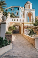 Un sendero que conduce a un edificio con fachada azul, una entrada en arco y una fuente decorativa.