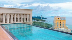 Una piscina en la azotea con vistas al mar y un edificio con columnas.