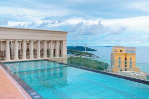 Una piscina en la azotea con vistas al mar y un edificio con columnas.