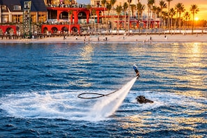 A jet ski performing a stunt with a person on board, water splashing around, and a beach with palm trees and buildings in the background. - Crystal Apartment Hillside Phu Quoc (Phu Quoc)