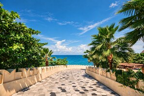 A paved pathway leading to a beach with palm trees and a clear blue sky. - Crystal Apartment Hillside Phu Quoc (Phu Quoc)