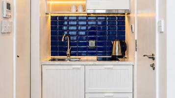A compact kitchen with white cabinetry, a blue tiled backsplash, and a wooden floor.