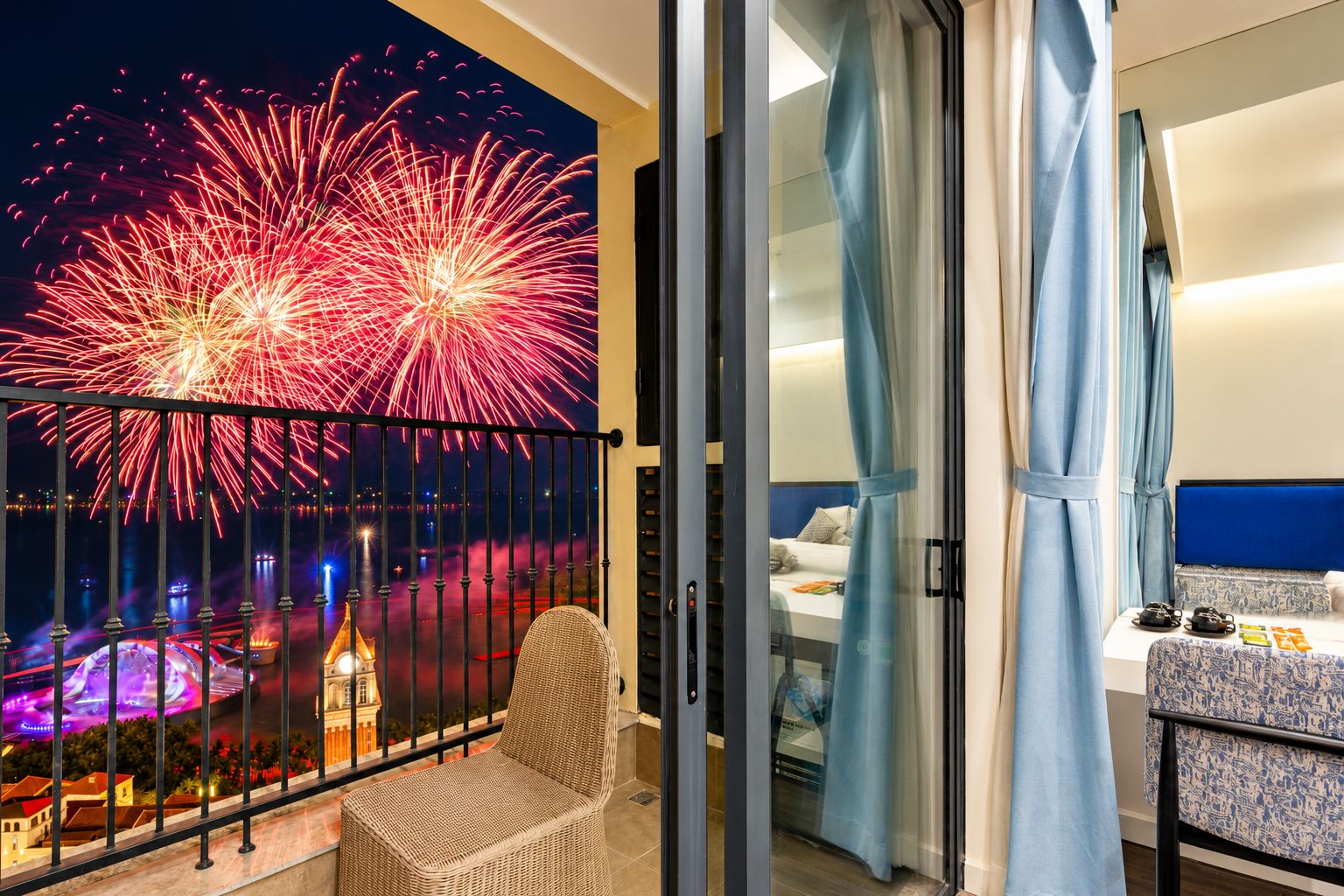 Varanda com vista de fogos de artifício, uma cadeira de vime e uma cama com cabeceira azul.