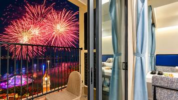 Varanda com vista de fogos de artifício, uma cadeira de vime e uma cama com cabeceira azul.