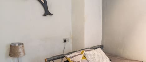 A bedroom with a bed, a bedside table with a lamp, a wall-mounted mirror, and a power outlet.