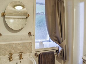 A bathroom with a white sink, two gold faucets, a mirror, and a window with a curtain. - 3 bedroom accommodation in Tremadog (Tremadog)