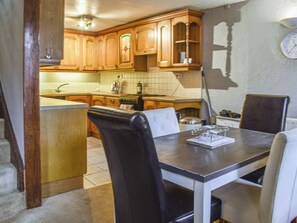 A kitchen with wooden cabinets, a dining table with chairs, and a clock on the wall. - 3 bedroom accommodation in Tremadog (Tremadog)