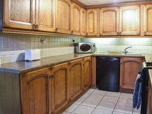 Una cocina con armarios de madera, microondas, lavavajillas y salpicadero de azulejos.
