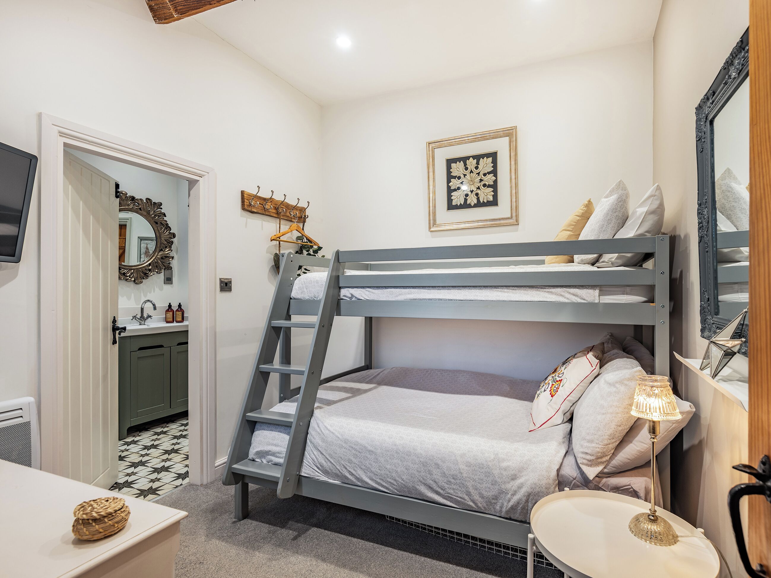 Una cama litera con escalera, una mesita de noche con lámpara, una obra de arte enmarcada en la pared y un espejo con un marco decorativo.