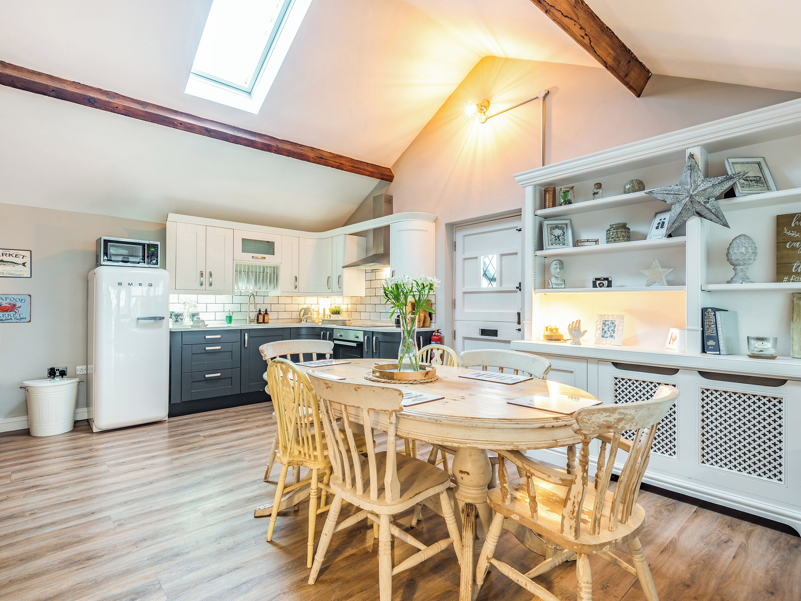 Une cuisine équipée d’une table à manger, de chaises, d’un réfrigérateur et d’une étagère où sont disposés des objets décoratifs.