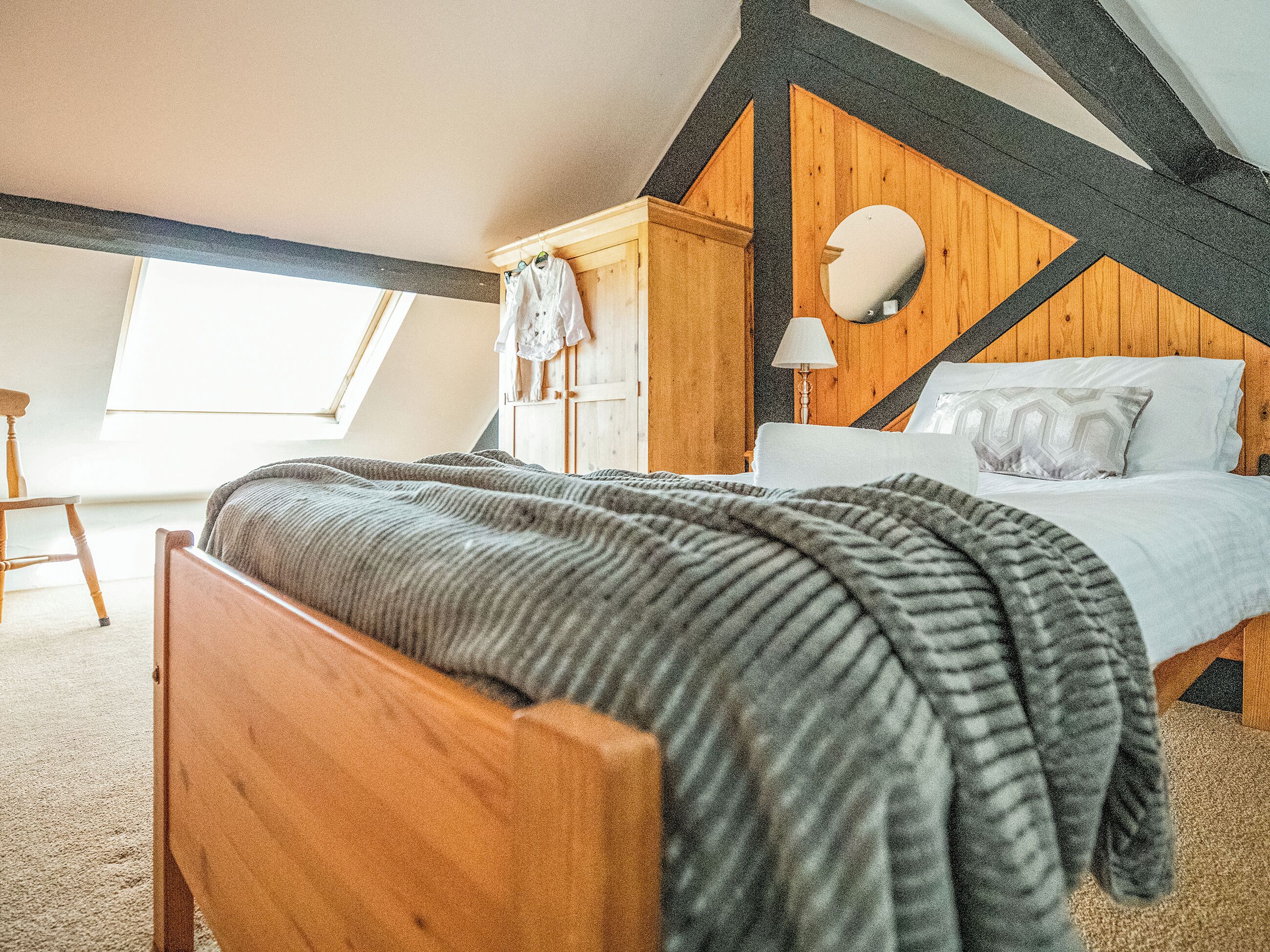 Een slaapkamer met een schuine kap, een houten bedframe, een groot raam en een kledingkast.