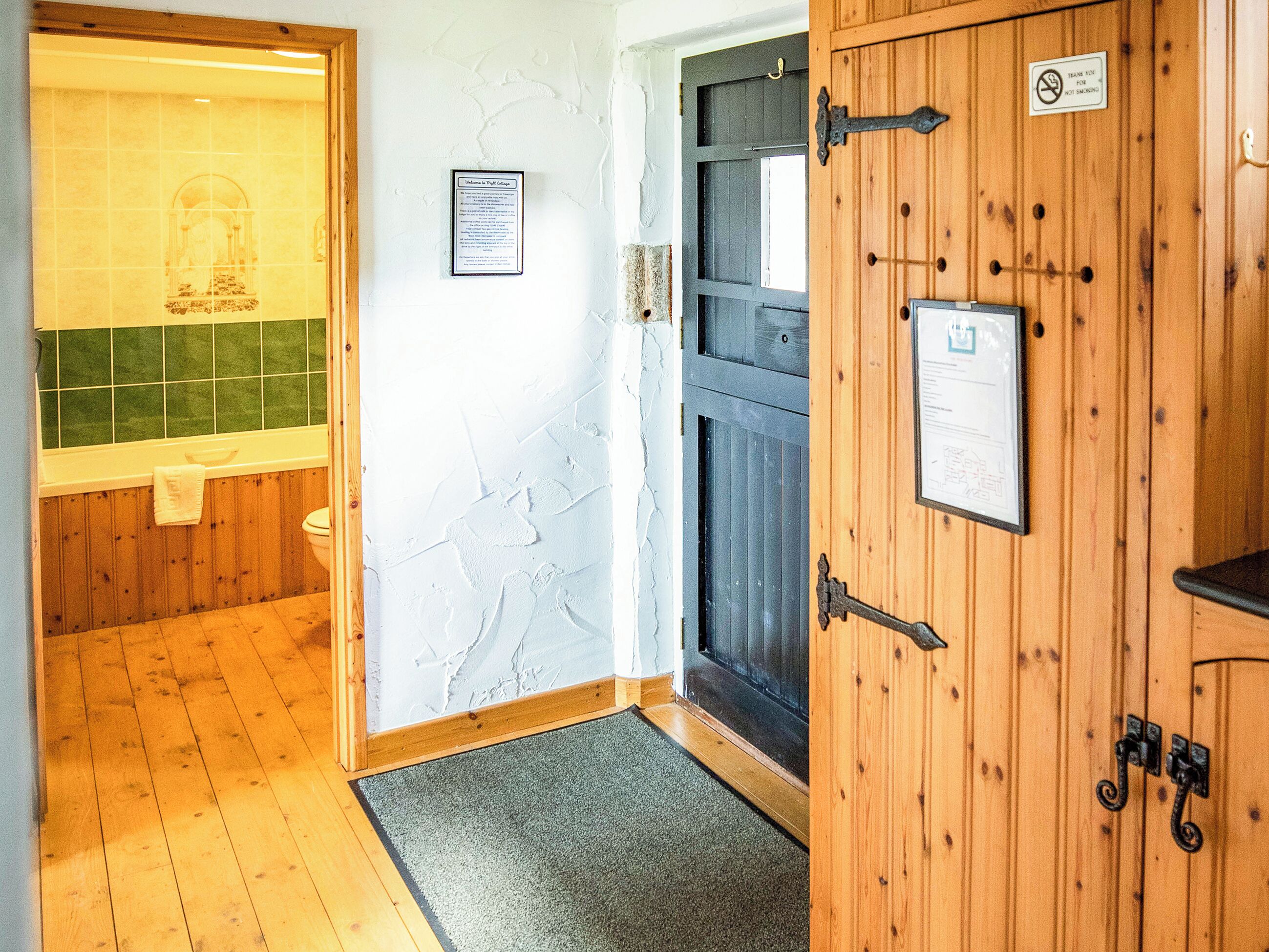 A bathroom with a wooden floor, a green tiled wall, a white sink, and a door with a no-smoking sign.