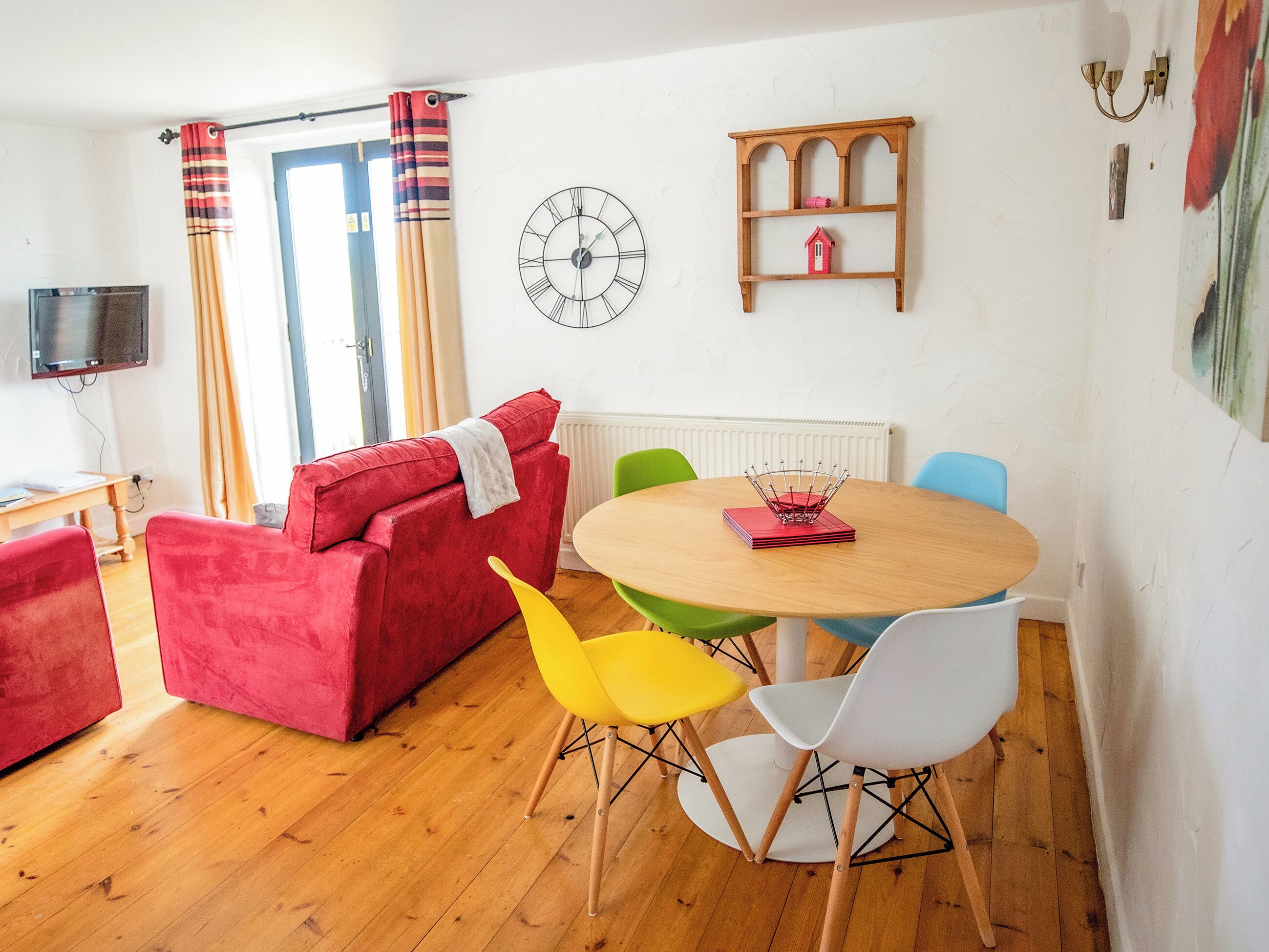 Un salon chaleureux avec un canapé rouge, une table à manger en bois et des chaises colorées.