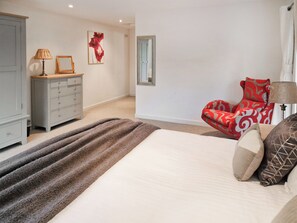 A bedroom with a bed, a red patterned chair, a grey dresser, and a mirror on the wall. - 1 bedroom accommodation in Crackington Haven (Crackington Haven)