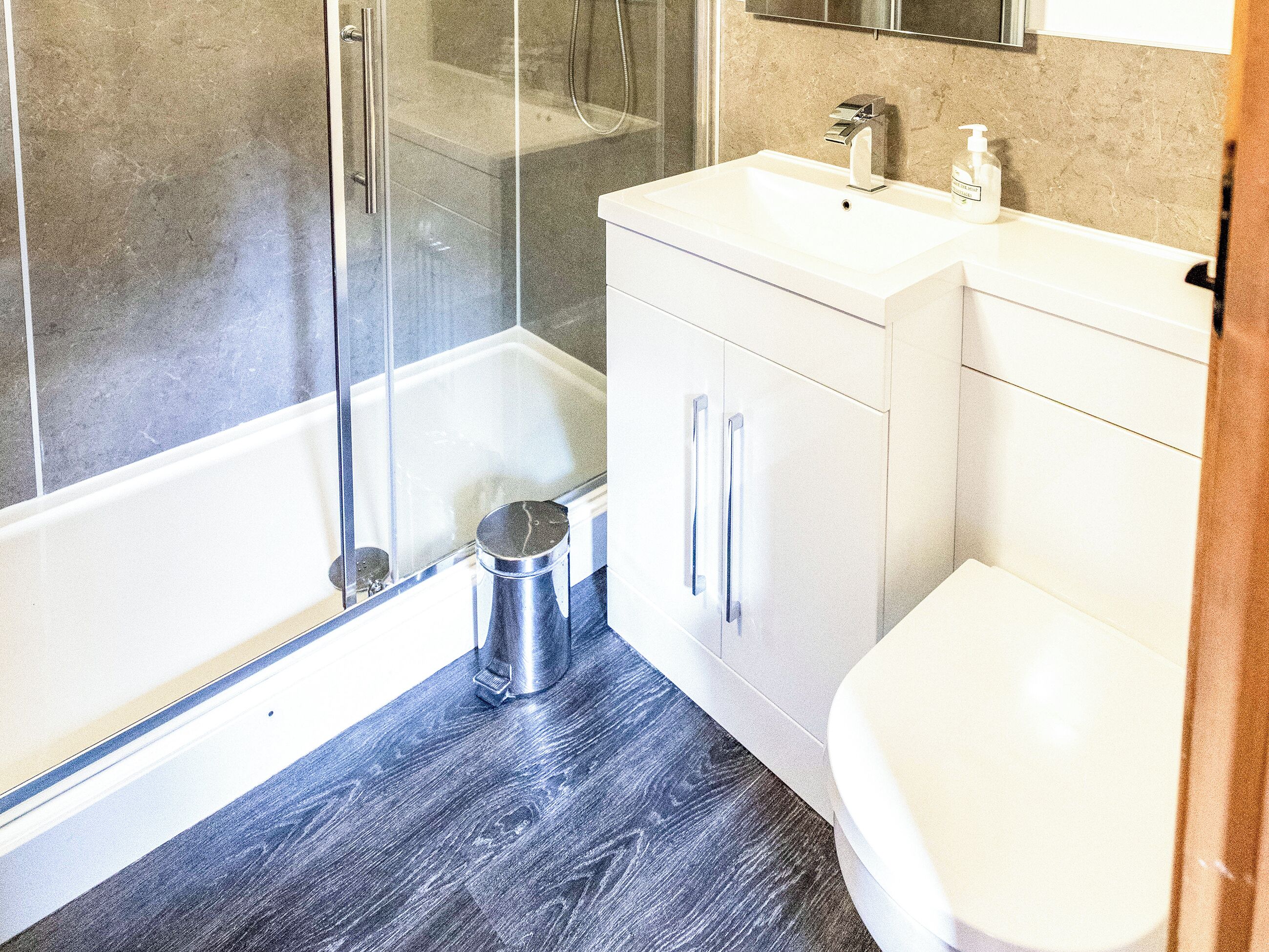 Une salle de bain moderne avec une douche à parois de verre, un lavabo blanc doté d’un distributeur de savon et des toilettes.