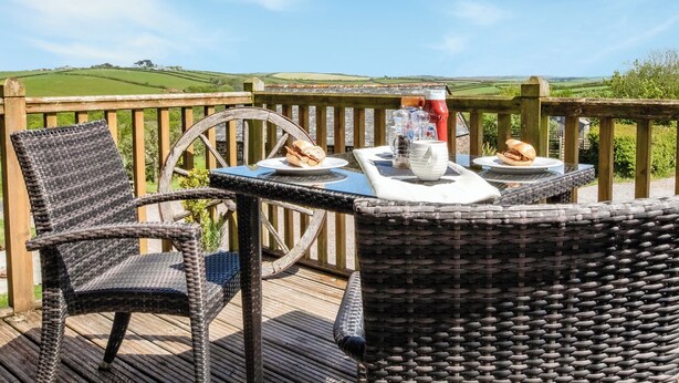Een rieten tafel met borden eten en toevoegingen op een terras met uitzicht op groene heuvels.