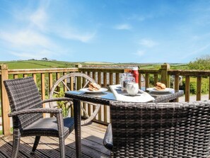 Een rieten tafel met borden eten en toevoegingen op een terras met uitzicht op groene heuvels.