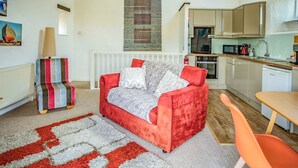 Een gezellig compacte ruimte met een rode bank, een gestreepte stoel, een kitchenette en een eettafel.