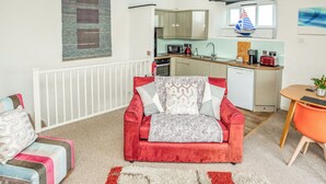 Een knus woongedeelte met een rode bank, een eettafel en een kitchenette op de achtergrond.