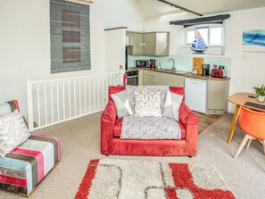 A compact living space with a red sofa, a small dining table, and a kitchenette in the background. - Butterwell - UK40046 (Crackington Haven)