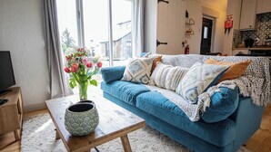 Ein Wohnzimmer mit einem blauen Sofa, einem Holztisch und einem Blumenstrauß.