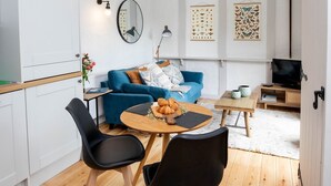 Ein modernes Wohnzimmer mit einem blauen Sofa, einem Holzes Esstisch mit zwei Stühlen, einer Küchenzeile und einem Fernseher.
