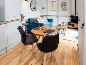Ett modernt vardagsrum med en blå soffa, ett matbord i trä med två stolar, en köksdel och en tv.