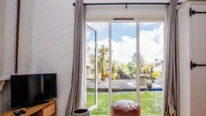 Ein Zimmer mit einer Holztv-Kommode, einem Tisch mit dekorativen Schalen und einer großen Schiebeglastür, die in einen Garten führt.