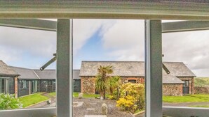 A view through a window with a stone building, a palm tree, and a clear sky. - 3 bedroom accommodation in Crackington Haven (Crackington Haven)