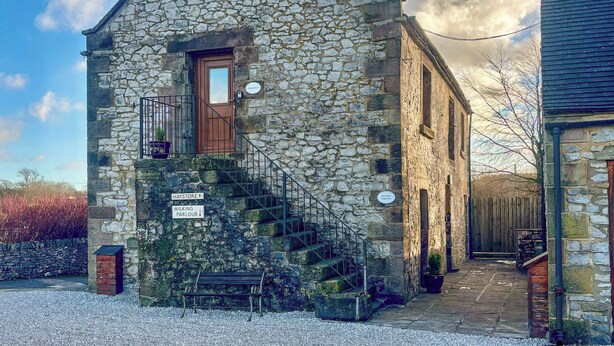 Un edificio de piedra con puerta de madera, una escalera y letreros que indican lugares cercanos como Haystore y Milking Parlour.