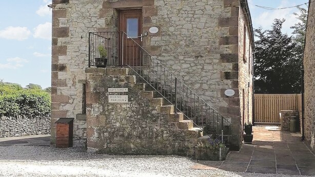 Un edificio de piedra con una escalera que lleva a una puerta, con letreros que indican 'Haystore', 'Milking' y 'Parlour'.
