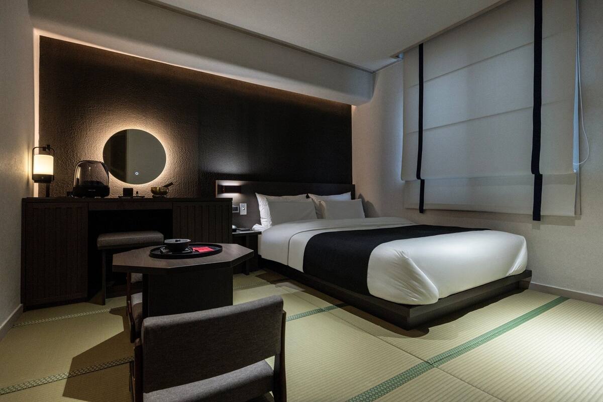 Habitación de hotel moderna con cama, mesita de noche, lámpara y vistas al exterior.