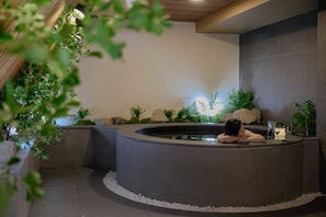 A spa area with a hot tub, surrounded by rocks and plants, and a person relaxing in the tub. - Cave Ryokan Hotel Anook Daejeon Yuseong (Daejeon)