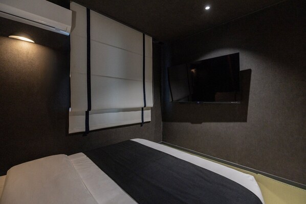 Une chambre avec un lit, un téléviseur fixé au mur et un luminaire au plafond.