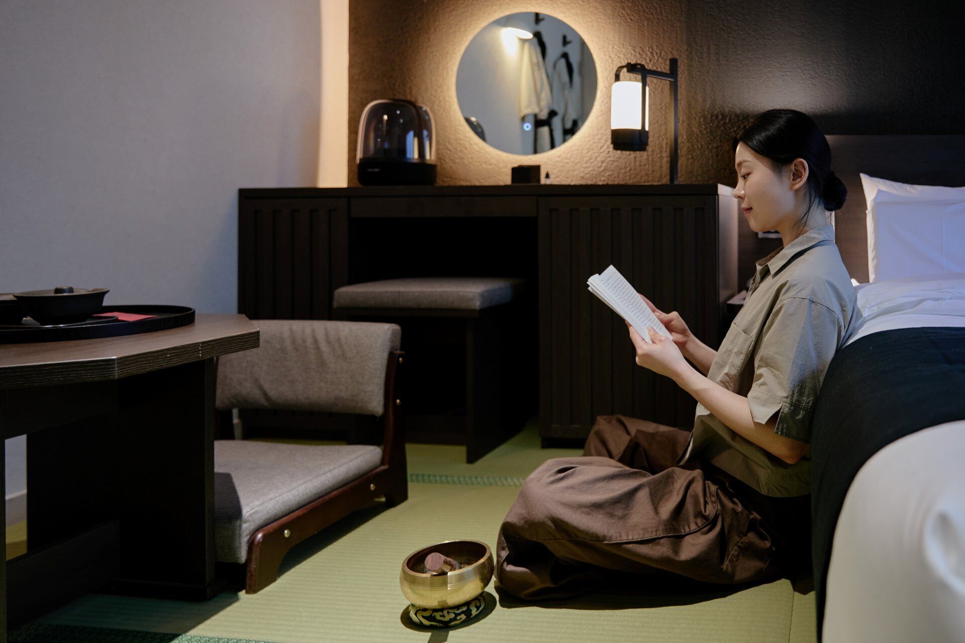 A room with tatami flooring, a low table with a tea set, a sofa, a small wooden stool, and a round mirror on the wall.