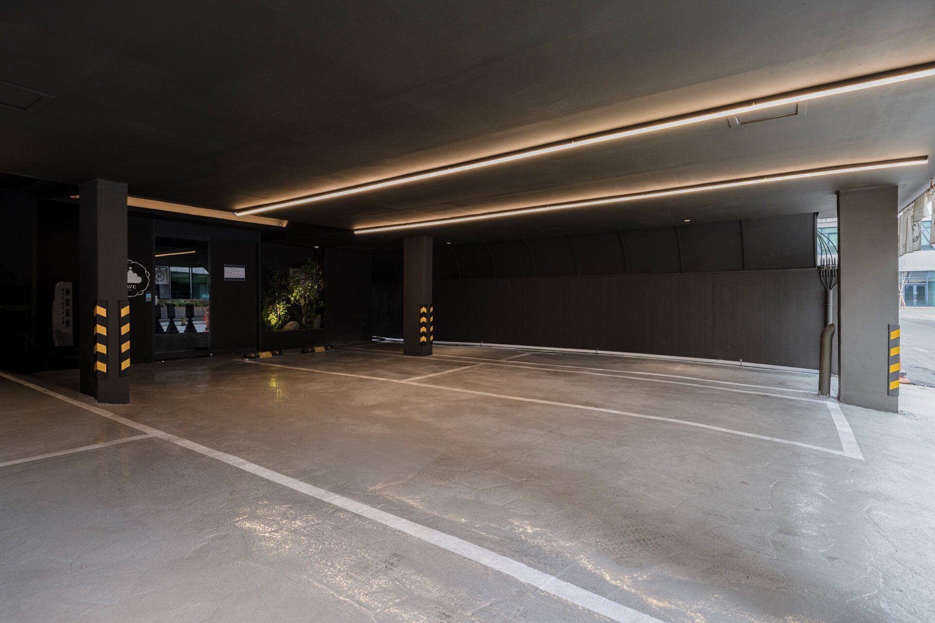 An underground parking garage with concrete floors, marked parking spaces, and illuminated ceiling lights.