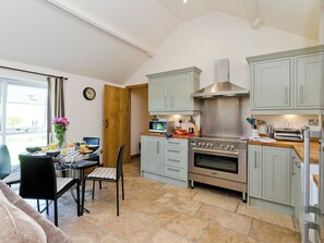 Une cuisine moderne avec des meubles gris, une cuisinière en acier inoxydable et un coin repas comprenant une table et des chaises.