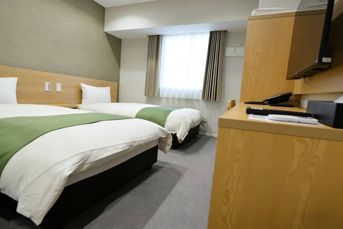 A hotel room with two beds, a desk with a telephone, and a window with curtains.