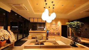 A modern hotel lobby with a reception desk, seating area, and a large wall mural. - Rita Hotel Namba (Osaka)