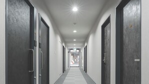 A long, narrow hallway with dark doors on both sides, a carpeted floor, and a ceiling light. - Rita Hotel Namba (Osaka)