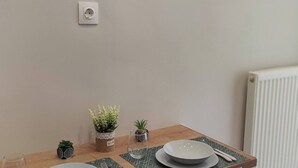 Un coin repas avec une table dressée pour deux personnes, un tableau encadré au mur et un radiateur en arrière-plan.
