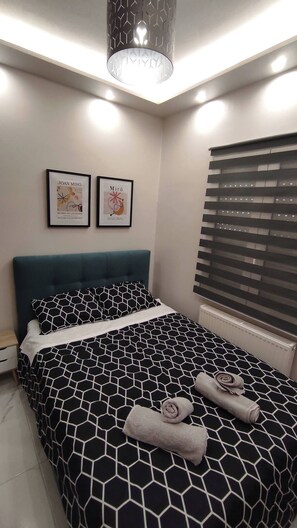 Un dormitorio moderno con una colcha de estampado geométrico, un cabecero color turquesa y dos cuadros enmarcados en la pared.