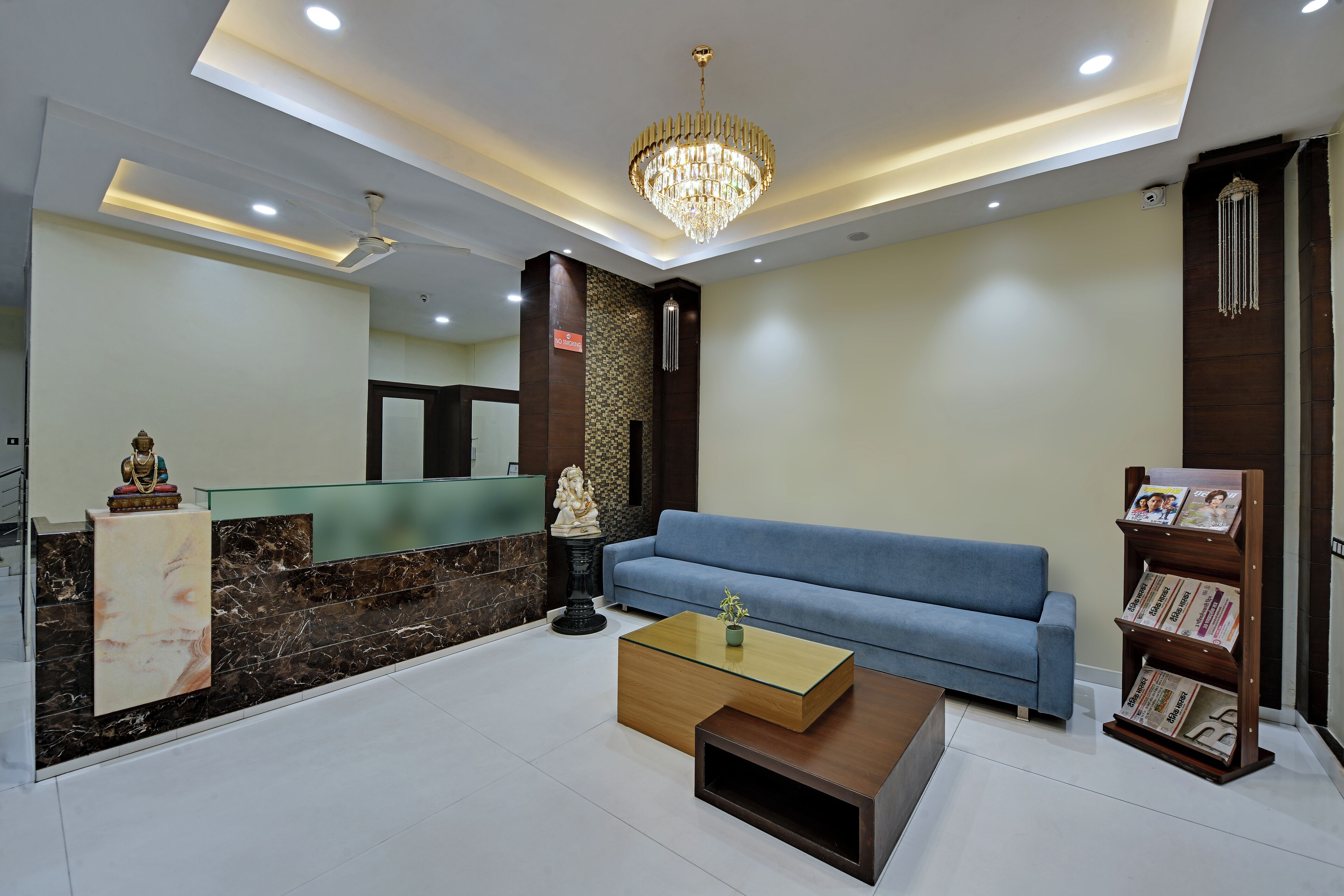 Zona de recepción con mostrador de mármol, sofá azul, mesa de centro de madera y candelabro.