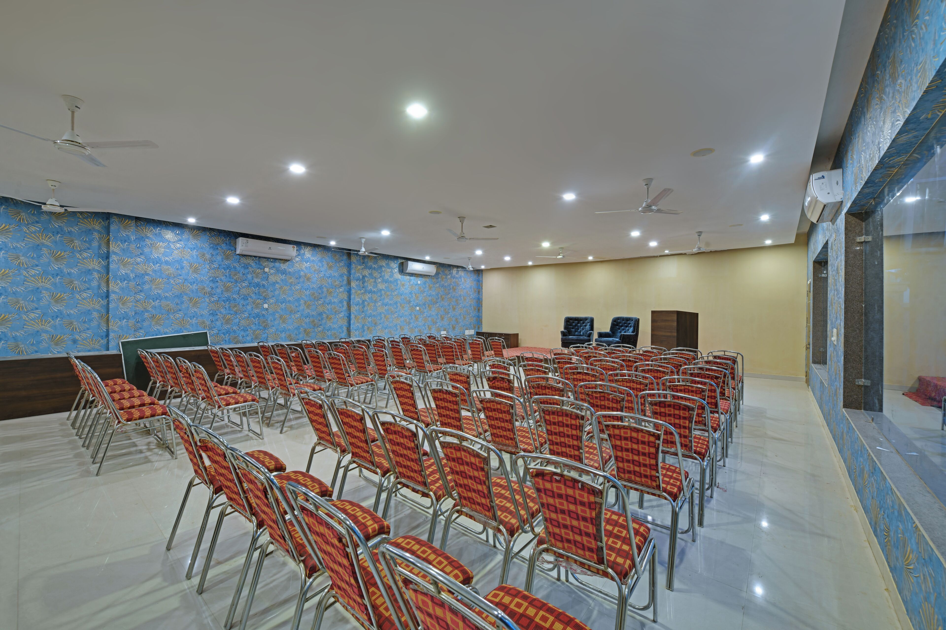 A conference room with rows of chairs, ceiling fans, and recessed lighting.