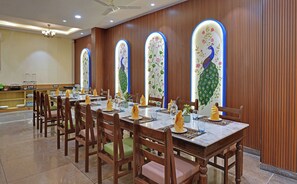 A dining area with wooden paneled walls, a chandelier, and a peacock-themed window.