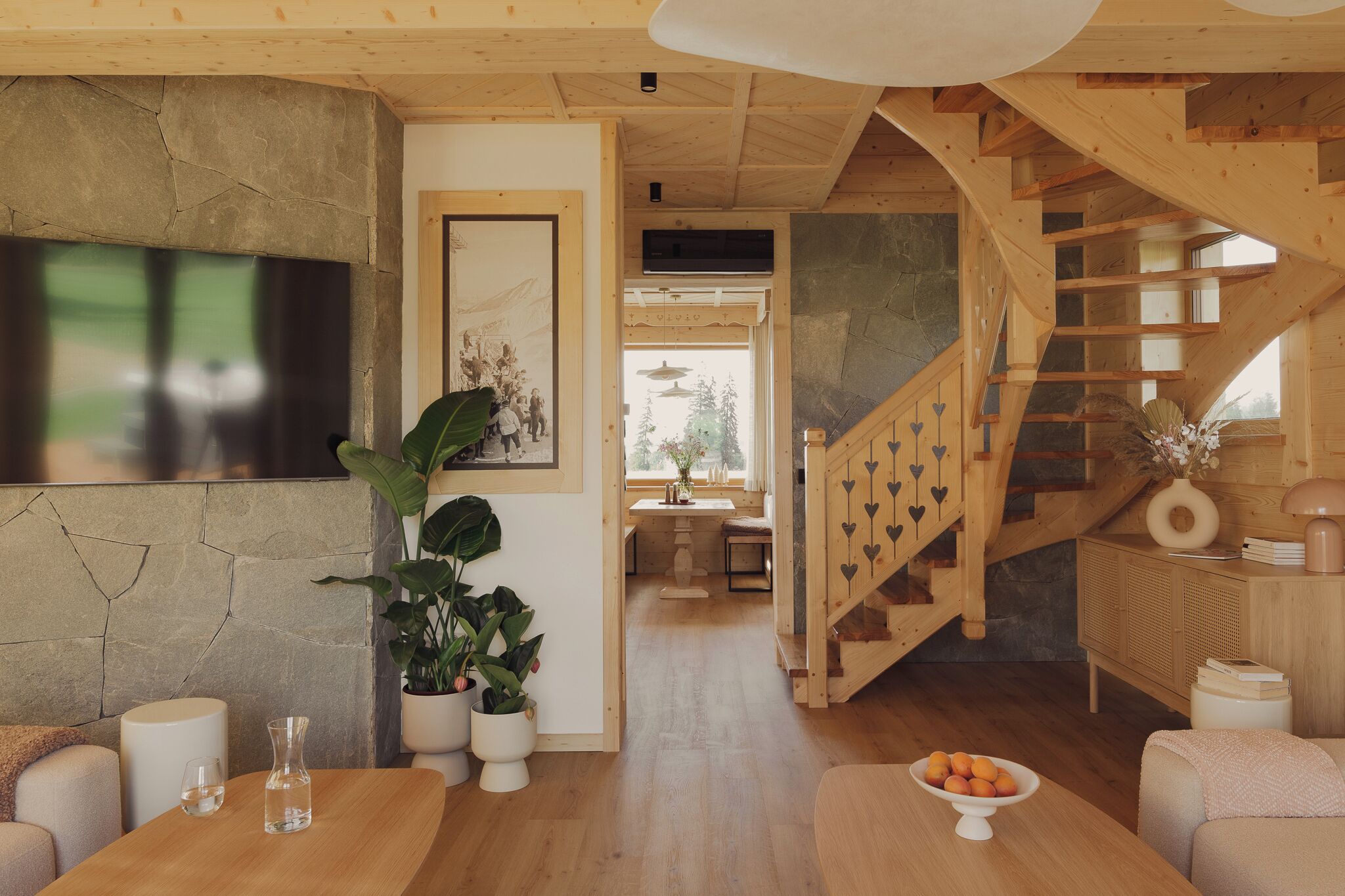 Un intérieur en bois comprenant un escalier, un coin repas et un espace de vie agrémenté de plantes et d’un téléviseur.