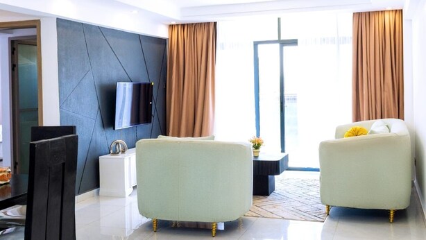 A modern living room with a flat-screen TV, two light-colored sofas, a dining table with chairs, and a large window with curtains. - Cozy 2-bedroom apartment in perfect Nairobi with fitness room WESTLANDS (Nairobi)