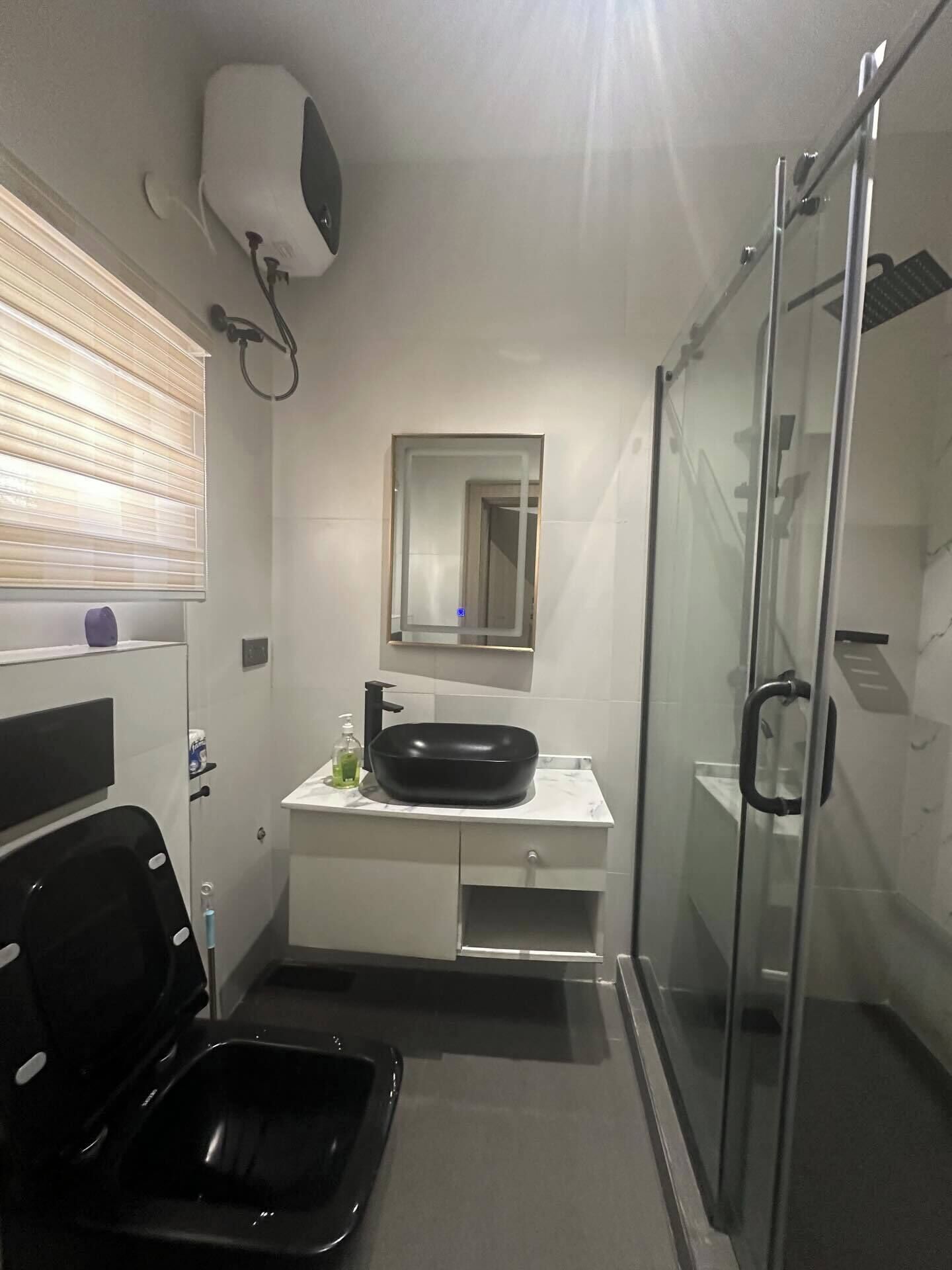 A compact bathroom with a black bathtub, a white vanity with a black sink, a glass shower enclosure, and a mirror above the sink.