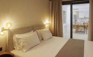 Une chambre d’hôtel avec un lit, deux lampes de chevet et une vue sur la salle à manger, accessible par une porte vitrée.