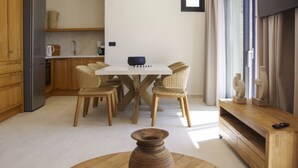 A modern kitchen with wooden cabinets, a white countertop, and a dining area with wicker chairs and a white table. - Villa Marenthe | 3 BDR | Sea Views | Pool | Syros (Syros)